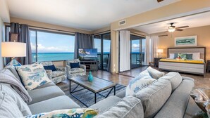 Een ruime woonkamer met een groot raam met uitzicht op de oceaan, een plafondventilator en een comfortabele zithoek met een bijzettafeltje.