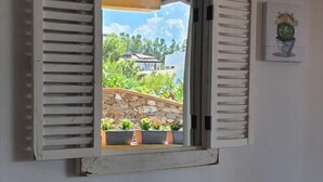 Ein Fenster mit Rollläden, Blick ins Grüne und ein kleiner Blumentopf an der Wand.