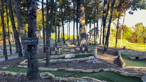 Um campo de mini golfe com uma placa que diz 'CHINOA-PUTT', rodeado por árvores.