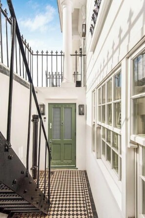 A narrow hallway with a green door, white walls, and a checkered floor.