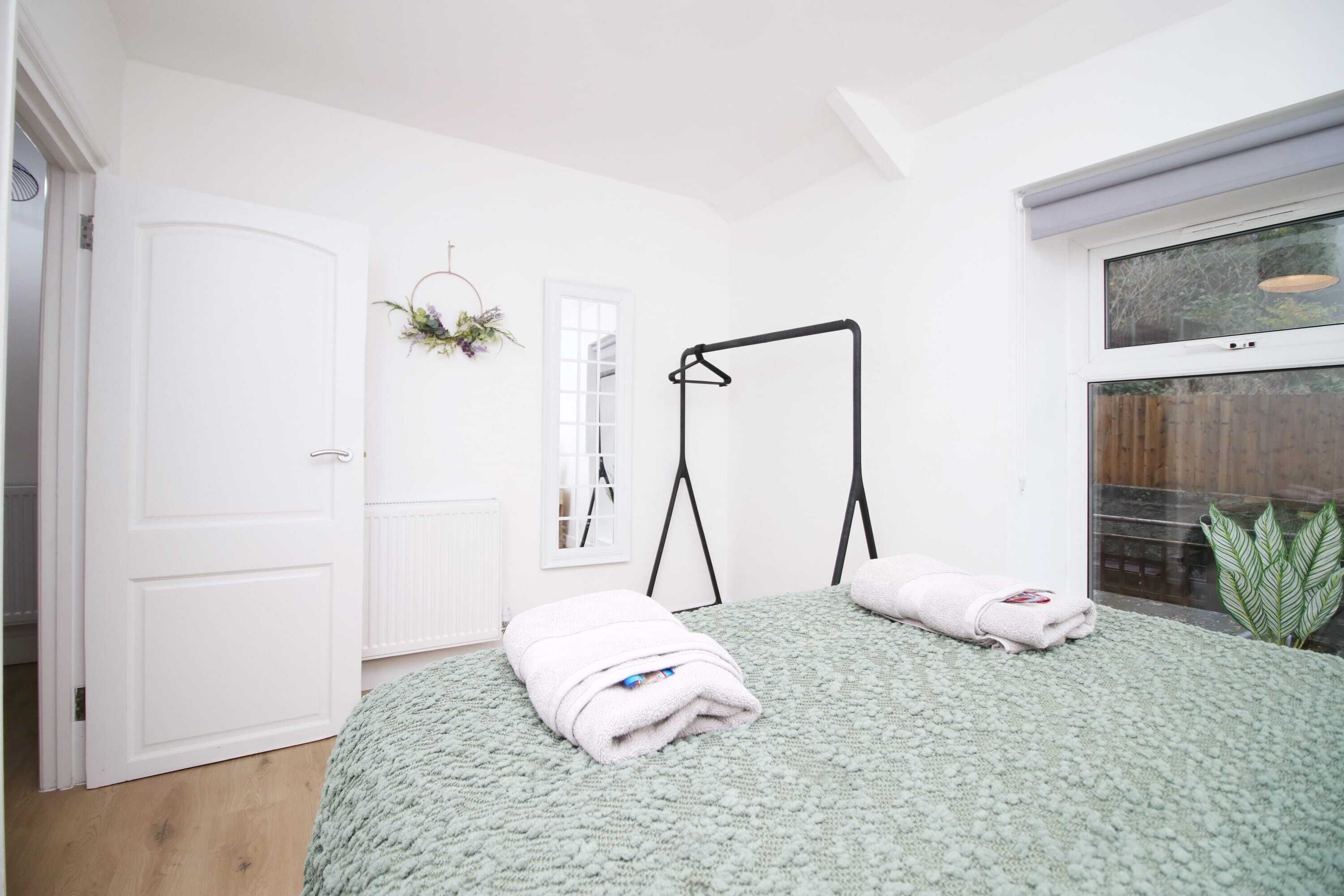A bedroom with a bed, a radiator, a window, a door, and a hanging plant.