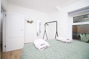 A bedroom with a bed, a radiator, a window, a door, and a hanging plant.