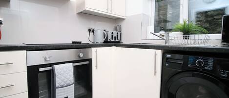 Una cocina compacta con horno integrado, lavadora y ventana con vistas a zonas verdes.