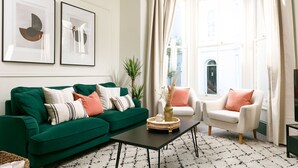 Un salon avec un canapé vert, un fauteuil blanc, une table basse et deux œuvres d’art abstraites encadrées accrochées au mur.