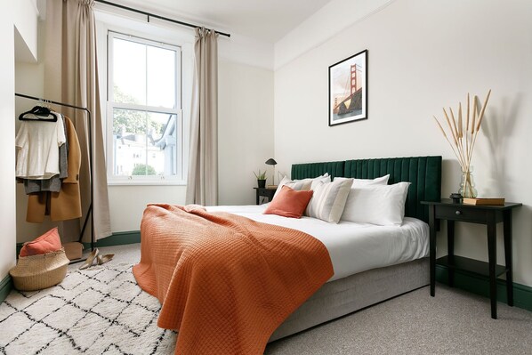 A bedroom with a bed, a window, a nightstand, a lamp, and a framed picture on the wall.