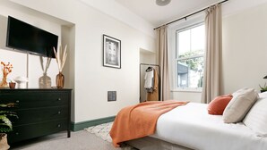 Een slaapkamer met een bed, een dressoir, een televisie en een raam met gordijnen.