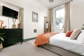 A bedroom with a bed, dresser, TV, and a window with curtains.