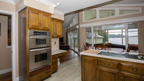 A kitchen with wooden cabinets, stainless steel appliances, and a large window overlooking a body of water. - Pinehurst Lake House Retreat - Pinehurst Lake Front Property With a Pool (Pinehurst)