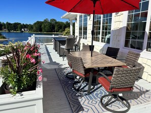 An outdoor patio with a wooden table and wicker chairs, overlooking a lake.