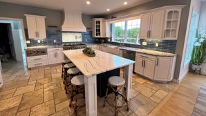 A modern kitchen with a central island, white cabinetry, and a large window providing natural light. - Huge Cape Cod Style Home on all Sandy beach / Cedar Lake MI (Oscoda)