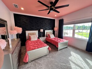 A bedroom with two beds, a ceiling fan, a dresser, and a window with a view of the outdoors.