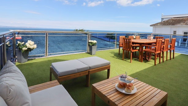 Une terrasse avec vue sur la mer, des meubles d’extérieur et une table où sont disposées des pâtisseries.