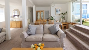 Un salon moderne avec un canapé beige, une table basse en bois et un coin repas comprenant un buffet en verre et des chaises en bois.