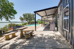 Eine überdachte Terrasse mit Gartenmöbeln, einem Pool und Blick auf den See.