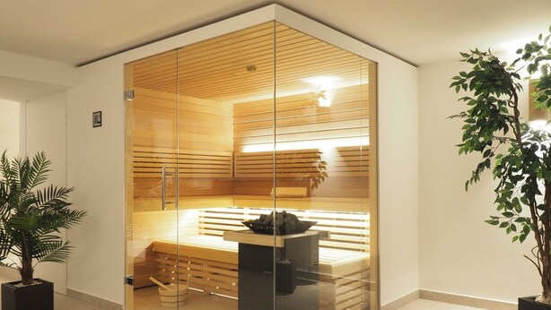 Un sauna moderne avec des murs en verre, des bancs en bois et un banc sur lequel se trouve un objet noir.