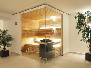 A modern sauna with glass walls, wooden benches, and a bench with a black object on it.