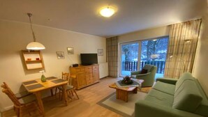 Un salon avec un canapé vert, une table à manger en bois et un téléviseur posé sur un meuble.