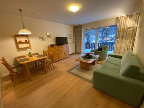 En stue med en grøn sofa, et træspisebord og et fjernsyn på et skab.