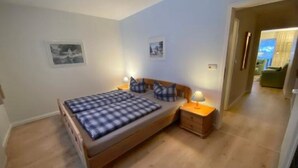 Une chambre à coucher avec un lit en bois, deux tables de chevet et une petite table de nuit. Deux tableaux encadrés sont accrochés au mur.