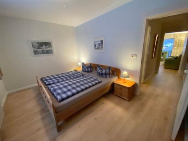 Een slaapkamer met een houten bed, twee nachtkastjes en een bedbank. Twee ingelijste foto’s hangen aan de muur.