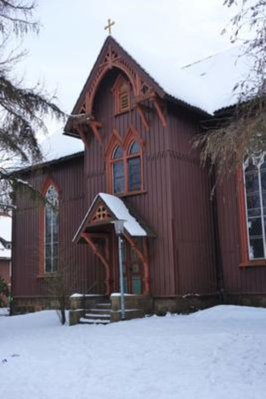 Eine Holzkirche mit einem steilen Satteldach und einem Kreuz auf der Spitze.