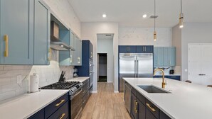 A modern kitchen with dark blue cabinets, stainless steel appliances, and a white countertop. - Homes by Villatel | Camping Theme BR, Sports Simulator, Theater, Gym, Near Parks (Davenport)