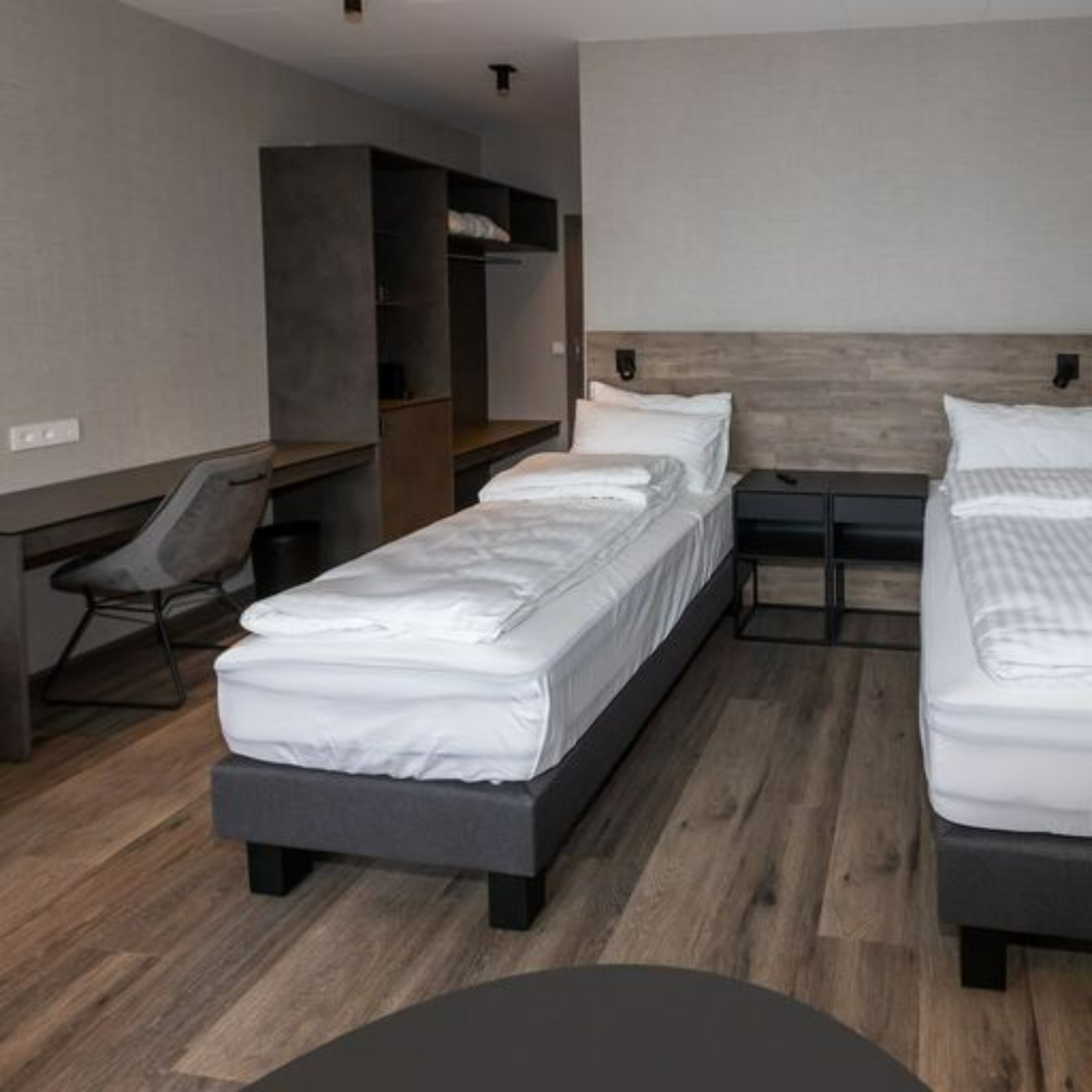 A modern hotel room with two single beds, a desk, and a chair.