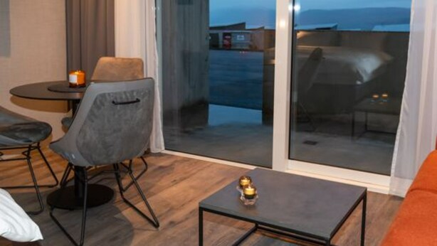 Una habitación moderna con sofá, una mesita y una silla. Cuenta con una puerta corrediza de vidrio que da a un espacio exterior.