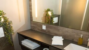 Un baño moderno con tocador de madera oscura, un lavabo blanco y un espejo grande.