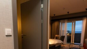 Habitación de hotel con cama, mesita de noche y vistas al exterior a través de un amplio ventanal.