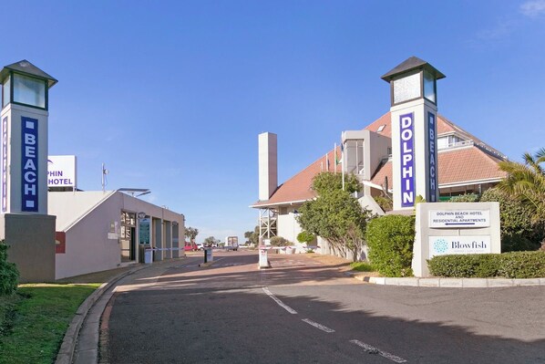 A hotel entrance with a clear sky, a road leading to the property, and signage for the Dolphin Beach Hotel and residential apartments. - Sea + Table Mountain Views at dolphin beach (Cape Town)