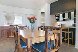 A modern kitchen with wooden cabinetry, a dining table with chairs, and a vase with flowers.