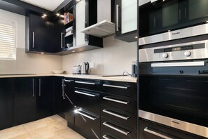 A modern kitchen with black cabinetry, stainless steel appliances, and a digital clock displaying 10:12. - Sea + Table Mountain Views at dolphin beach (Cape Town)