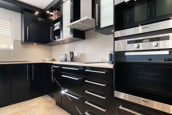 A modern kitchen with black cabinetry, stainless steel appliances, and a digital clock displaying 10:12.