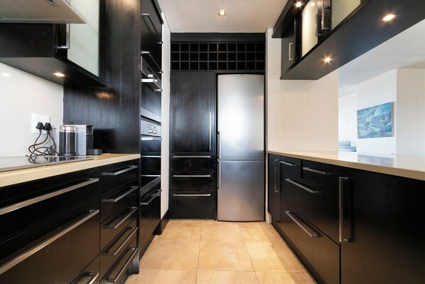 A modern kitchen with black cabinetry, stainless steel appliances, and a tiled floor.