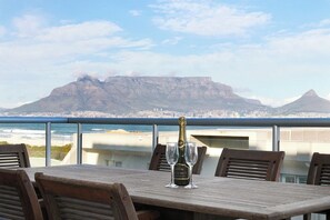 A table with a bottle of champagne and glasses on a balcony overlooking a city and mountains.