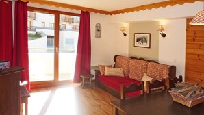 A cozy room with a wooden floor, a red sofa, a wooden table, and a view through a glass door. - Resort center, 1st floor, swimming pool, sauna, balcony, tv, ski locker, 50m², Les Orres (Les Orres)