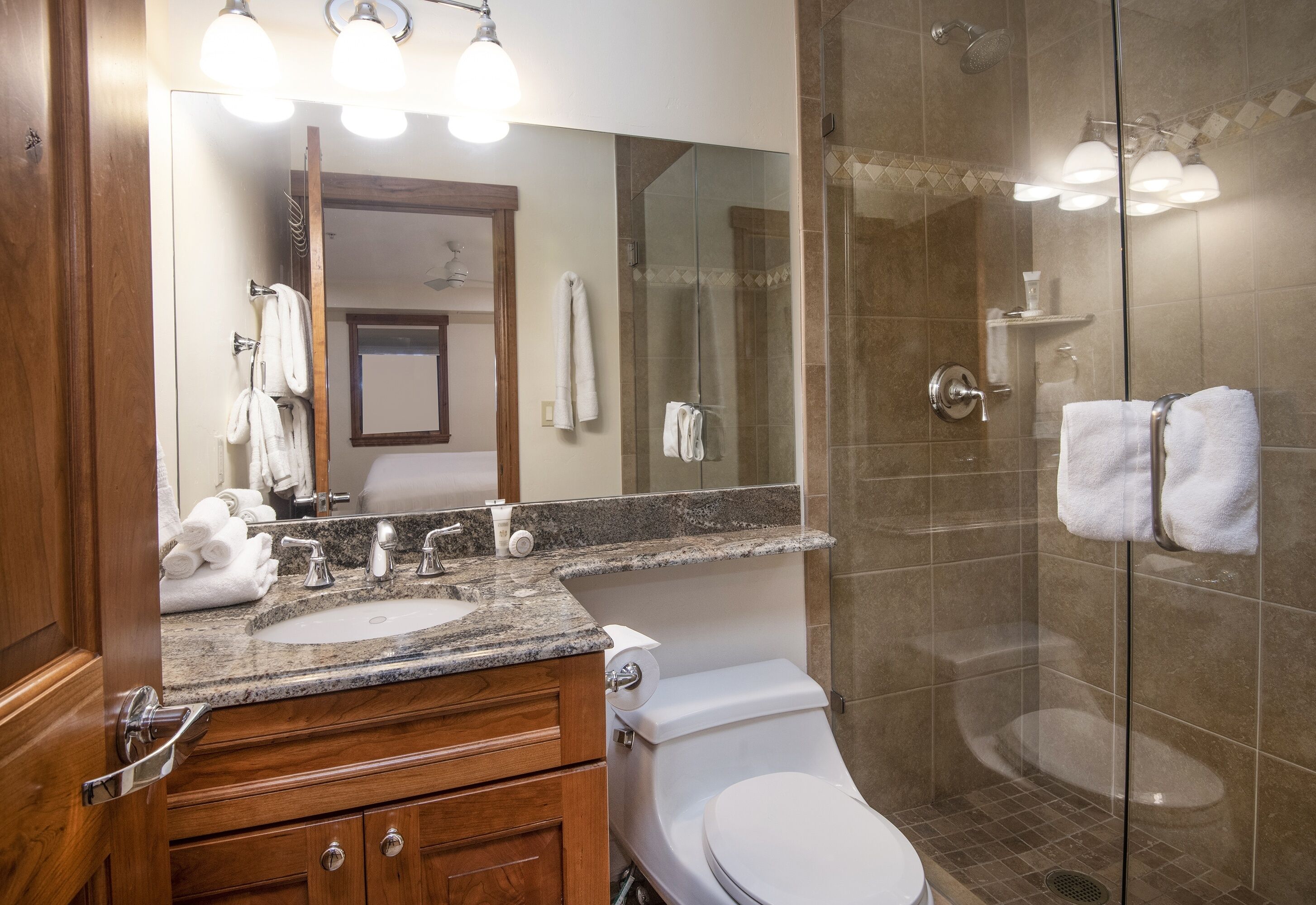A modern bathroom with a granite countertop, a white sink, a toilet, and a glass-enclosed shower area.