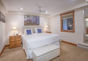 Un dormitorio con una cama grande, dos mesitas de noche, un ventilador de techo, una ventana y un espejo.