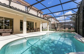 A swimming pool with a covered patio area, outdoor furniture, and a view of a residential building. - Beautiful 9 bedroom pool home located in the Solterra Resort! 9 Home by RedAwning (Davenport)