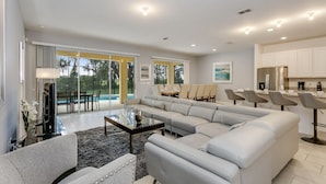 A modern living room with a sectional sofa, a glass coffee table, and a dining area with chairs. - Beautiful 9 bedroom pool home located in the Solterra Resort! 9 Home by RedAwning (Davenport)