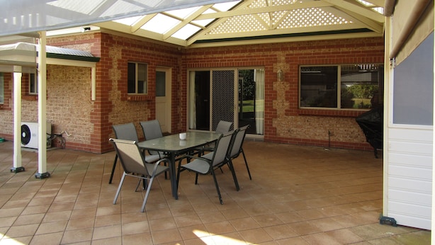 Un patio couvert avec un mur en briques, une table avec des chaises et un barbecue.