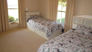 Une chambre avec deux lits simples, un ventilateur de plafond et de grandes fenêtres avec des rideaux.