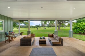 A covered patio with wicker furniture, a coffee table, and a view of a golf course.