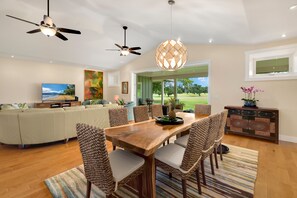 A modern living room with a wooden dining table, wicker chairs, and a ceiling fan.