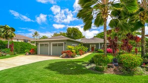 A residential house with a well-maintained lawn, a driveway, and a variety of colorful plants and flowers. - Hale Alaula, Elegant Hawaiian Home at exclusive Sunset Drive (Princeville)