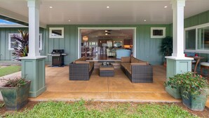 A covered outdoor seating area with wicker furniture, a grill, and potted plants. - Hale Alaula, Elegant Hawaiian Home at exclusive Sunset Drive (Princeville)