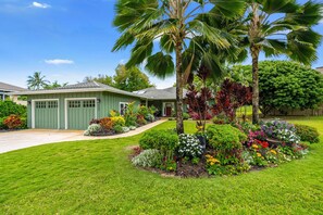 A green house with a well-maintained lawn and various colorful plants.