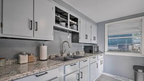 A modern kitchen with white cabinets, granite countertops, and a window with blinds. - 11 Mi to Dtwn Branson: Cottage in Rockaway Beach! (Rockaway Beach)