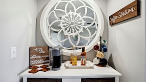 Een koffiehoek met een decoratief raam, een Keurig koffiezetapparaat en een dienblad met koffiemokken en flessen.